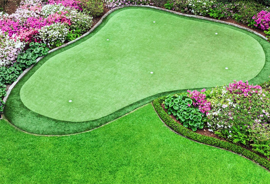 Residential putting green installation with flower beds and custom outdoor landscape design.
