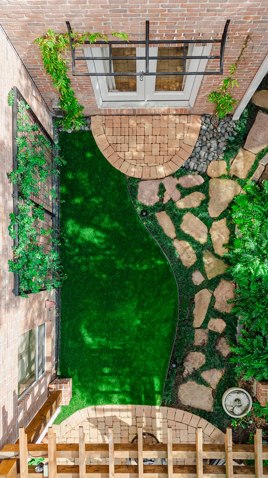 Aerial view of a residential courtyard featuring curved lawn design, natural stone pathways, and brick patio details.