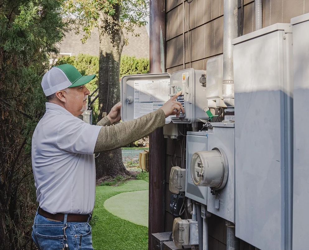 Hogue Landscape Services crew member inspecting a sprinkler system control box during irrigation maintenance.