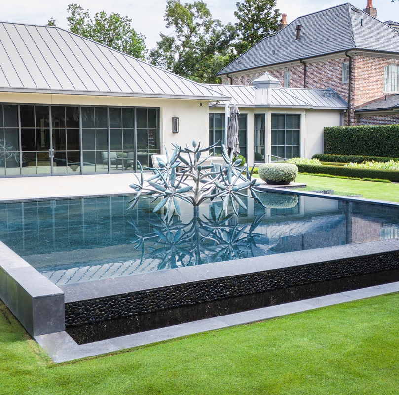 Luxury outdoor living space featuring a modern pool, sculptural water feature, and formal garden landscaping.