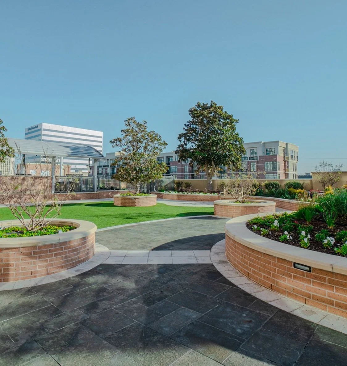 Modern rooftop outdoor space with lush turf, architectural brick planter beds, and elevated tree landscaping.