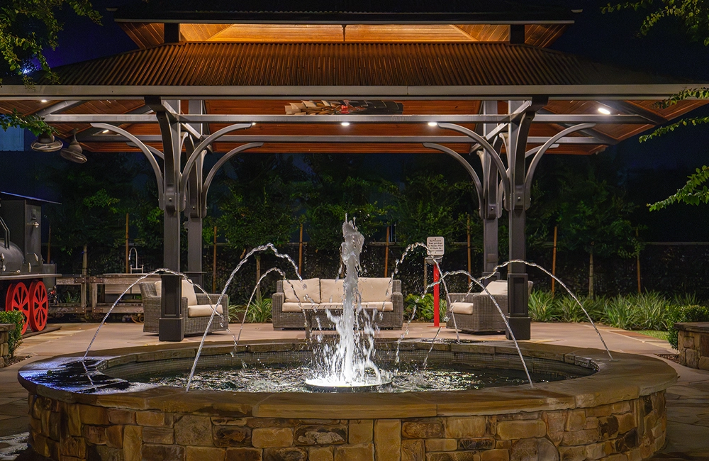 Outdoor patio and water feature illuminated with warm landscape lighting for nighttime outdoor living.