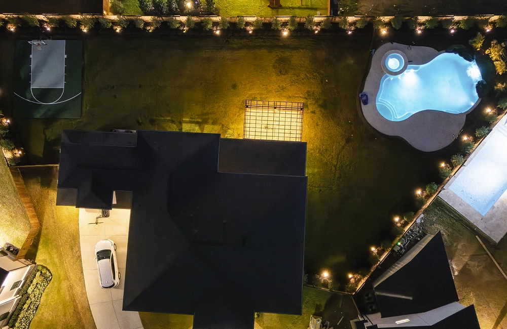 Aerial nighttime view of a residential property featuring smart landscape lighting and illuminated outdoor living spaces.